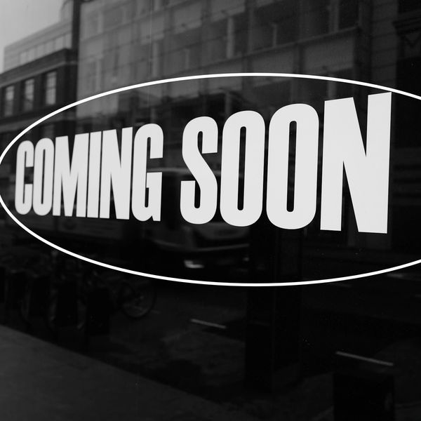 A bold "COMING SOON" sign on a window with a city street reflection.