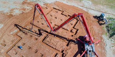 A red concrete pump truck working on a construction site with foundation trenches.