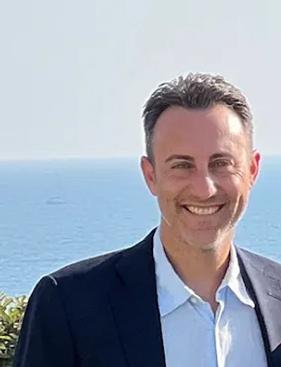 Smiling man in a suit with ocean background.