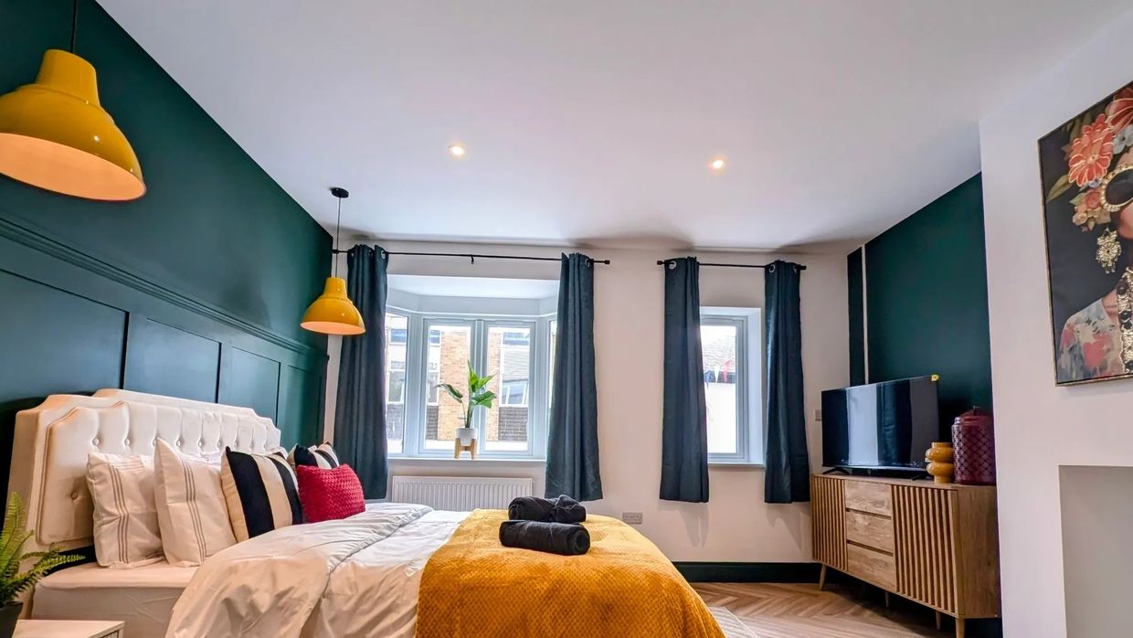Modern bedroom with yellow accents and dark curtains.