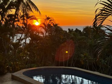 Sunset over a tropical pool surrounded by palm trees.