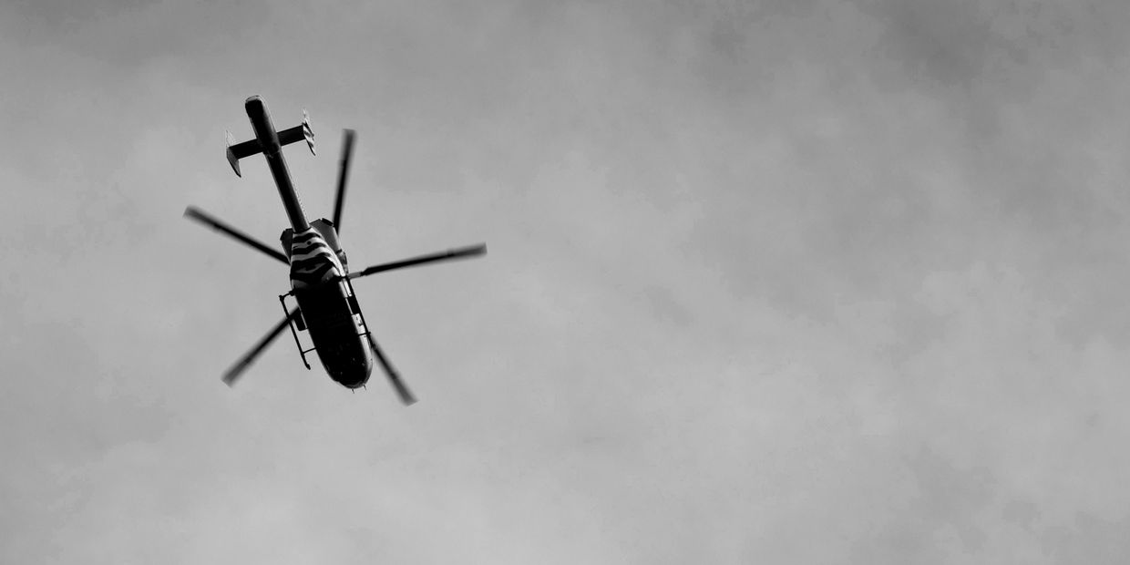 Black and white photo of a helicopter flying overhead against a cloudy sky.