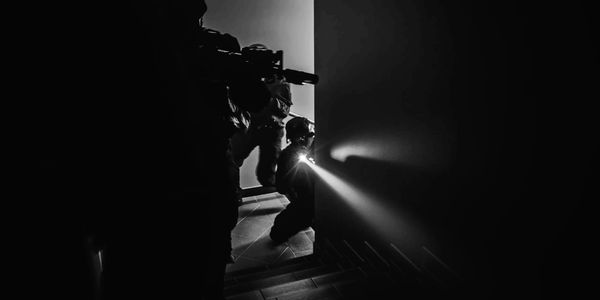 Tactical team with flashlights and weapons advancing in a dark stairwell.