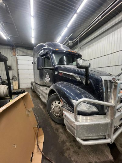 A large black semi-truck parked inside a garage with bright ceiling lights.