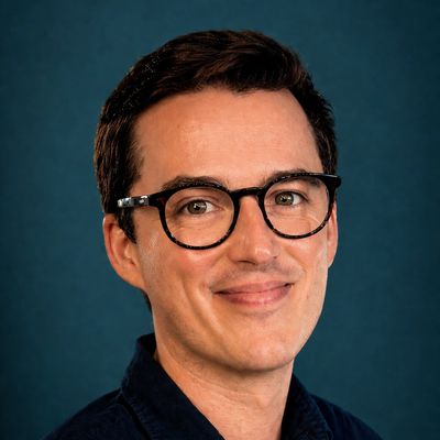 Smiling man with glasses against a dark blue background.