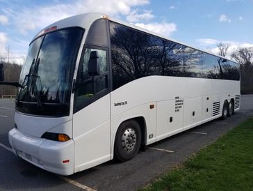 A white coach bus parked on the side of a road under a blue sky.