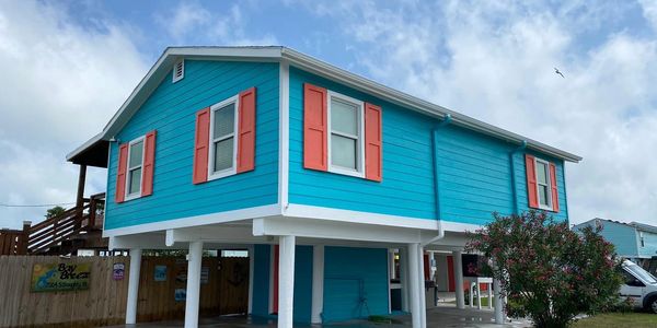 Coastal-style elevated house painted in bold aqua blue with crisp white trim with orange-red window.