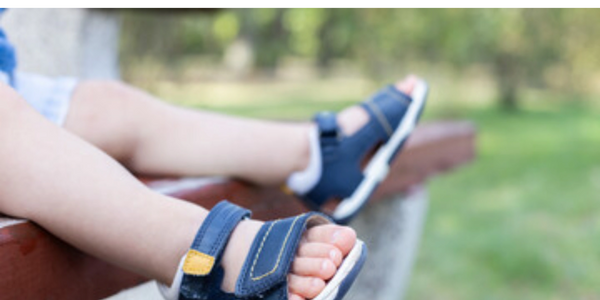 toddlers feet in blue sandals, blurred bench seat in background.  
