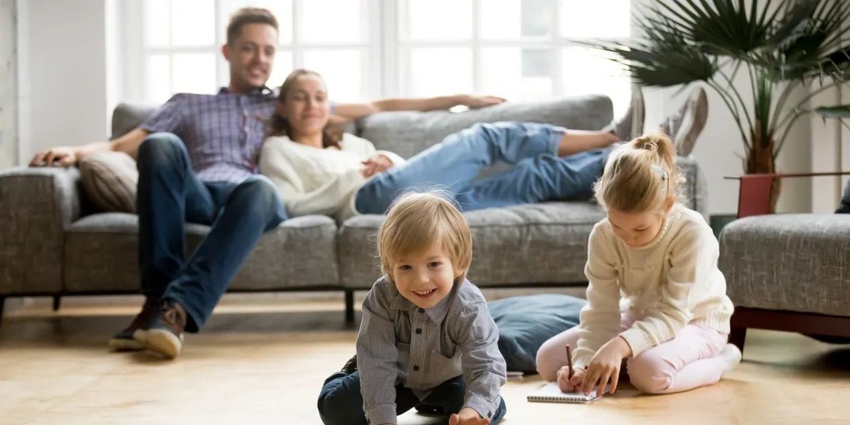 Happy kids playing on the floor while parents relax on the couch.