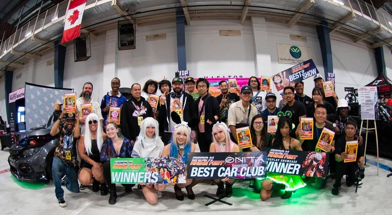 Group photo of anime fest winners holding awards and banners in a convention hall.