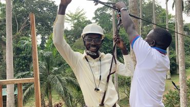 Two men preparing for a zip line adventure in a tropical setting.