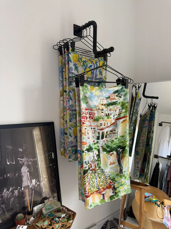 Colorful printed fabrics hang on a metal rack against a white wall.