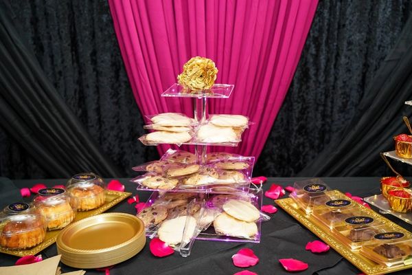 Elegant dessert table with cookies and cupcakes, adorned with rose petals and vibrant drapes.