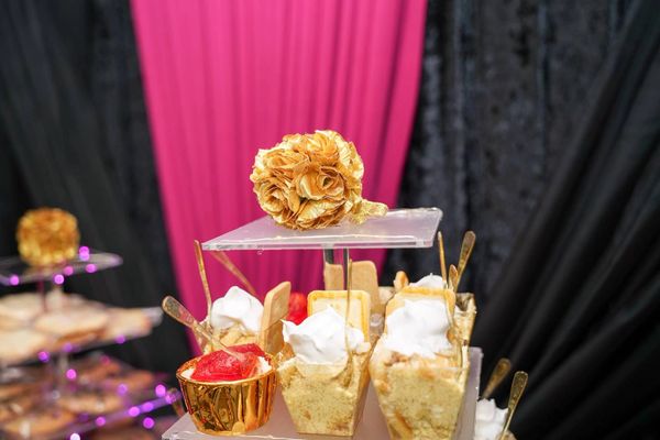 Elegant dessert display with gold and white theme against pink and black backdrop.