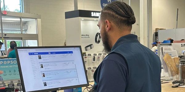 Man working on a computer at a store counter with tech products in the background.