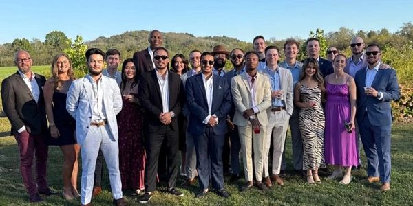 Group of well-dressed people posing outdoors on a sunny day.