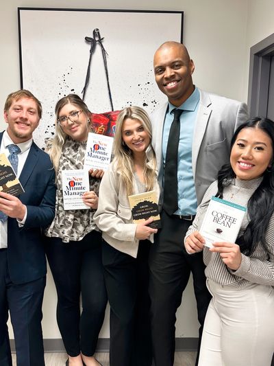 Five professionals smiling and holding books in an office setting.