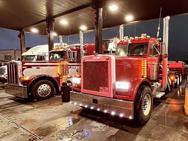 Several of Semper Fi transports semi trucks fueling up at night for a long haul