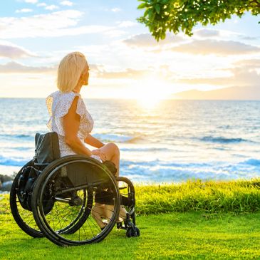 Woman in wheelchair watching a beautiful sunset by the ocean.