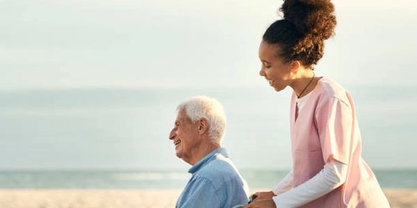 Young caregiver pushing elderly man in wheelchair on the beach.