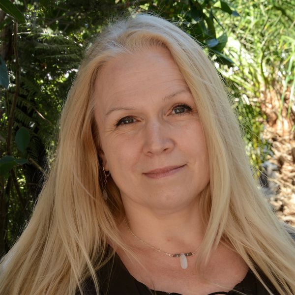 Smiling woman with long blonde hair in a natural outdoor setting.