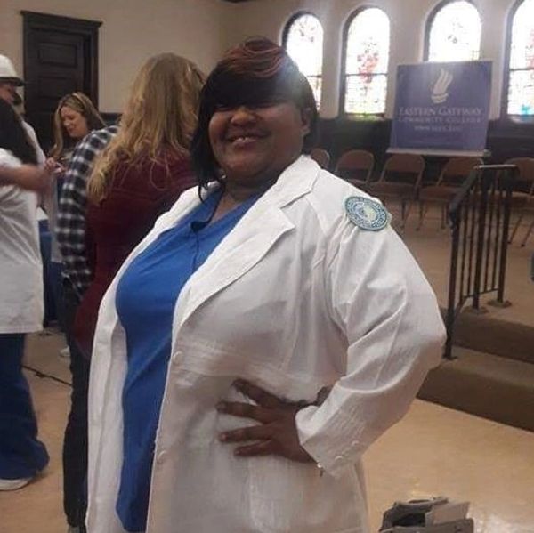 A smiling woman in a blue outfit and white coat posing indoors.