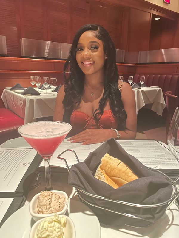 Smiling woman dining with bread and cocktail at a restaurant.