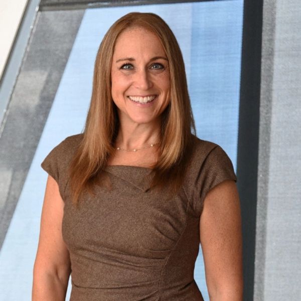 Tara Cunningham, a blond haired white woman smiling against an angled window.