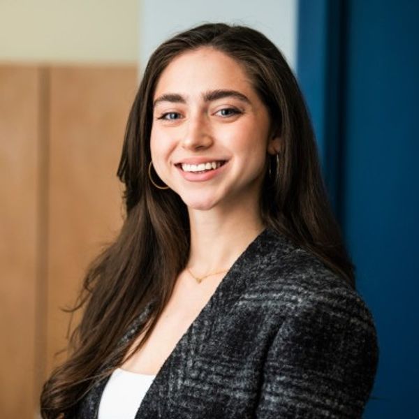 Cybil Seneker, a brown haired white woman smiling against a blue wall.