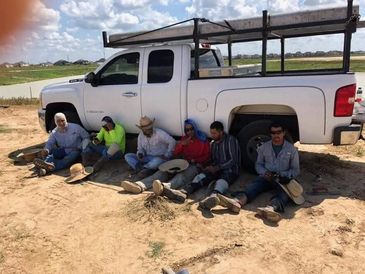 Six workers resting in the shade beside a white pickup truck on a sunny day.