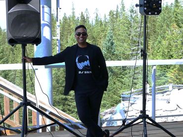 smiling vancouver dj standing beside dj speaker, lighting and equipment