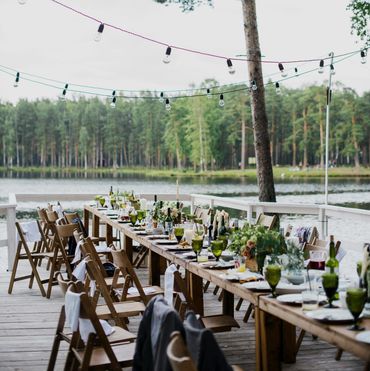 long table on boardwalk with plates, glasses and flowers with view of water