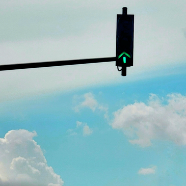 Traffic light showing green arrow against a blue sky with clouds.