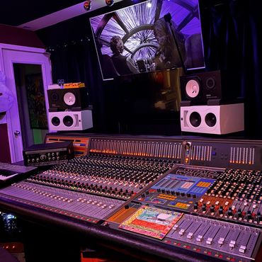A music studio with a mixing console and a Star Wars scene on the screen.