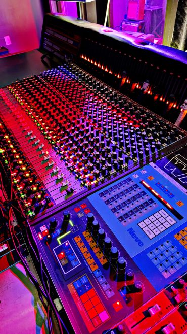 Close-up of a vibrant Neve audio mixing console with colorful lighting.