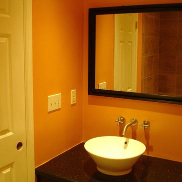 Bathroom with orange walls, a black framed mirror, a white vessel sink on a black granite countertop