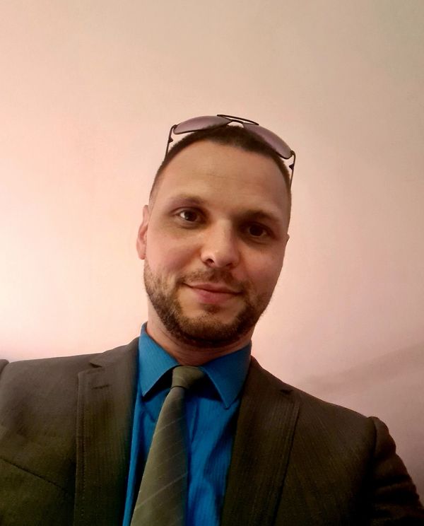 Man in suit with blue shirt and tie, wearing sunglasses on his head.