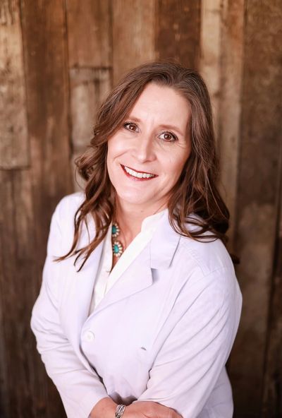 Smiling woman in a white coat against a rustic wooden background.