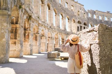 A woman in a straw hat explores ancient stone ruins on a sunny day.