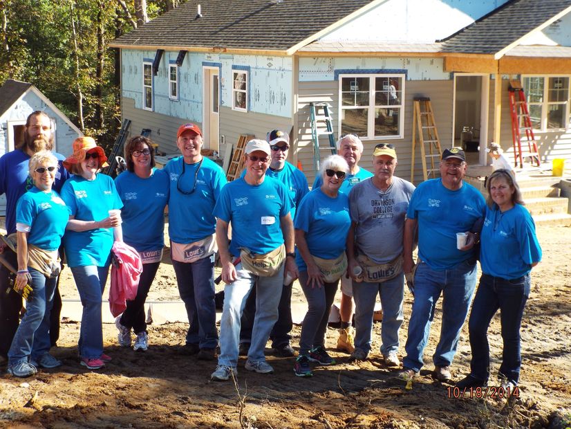Group of volunteers wearing blue shirts posing in front of a house under construction.