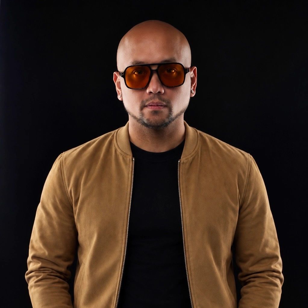 Man with sunglasses in brown jacket against black background.