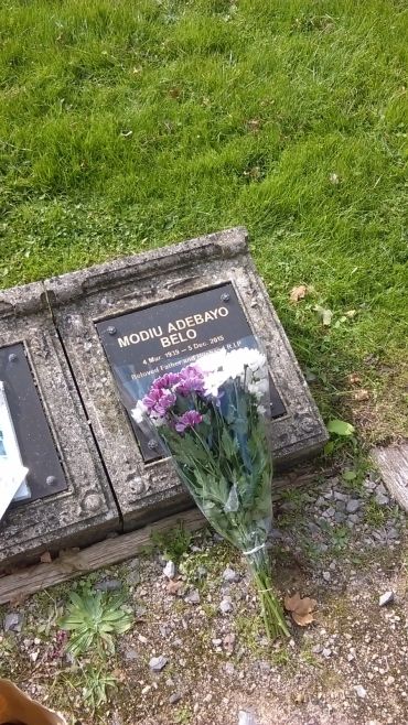 A grave plaque with flowers placed on it in a grassy cemetery.