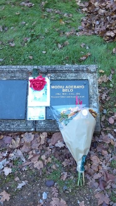 Grave of Modiu Adebayo Belo with flowers and a red rose on the plaque.