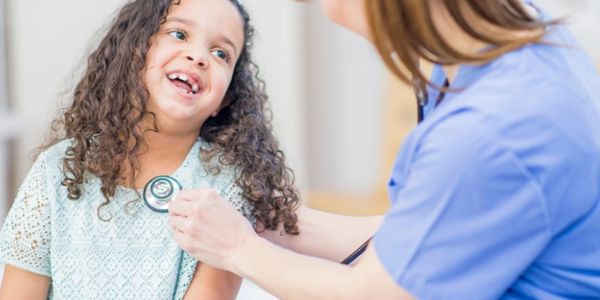 A child smiling as a doctor listens to her heartbeat with a stethoscope.