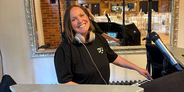 Smiling DJ with headphones at a keyboard in a warmly lit venue.