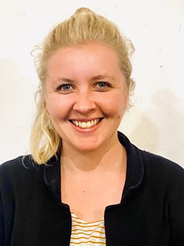 Smiling woman with blonde hair and blue eyes wearing a black jacket.