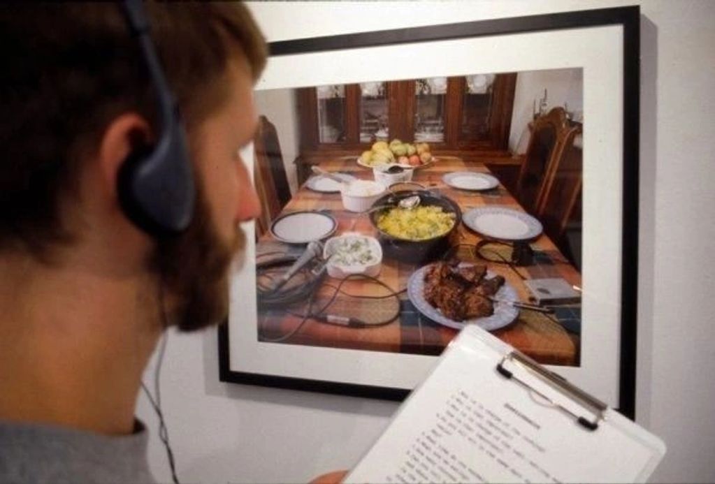 Man observing a photo of a dinner table with headphones and clipboard.