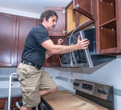 Man installing a microwave above the stove.