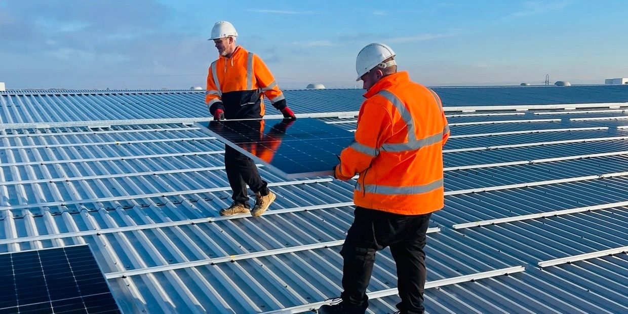 2 workers carrying a new solar panel across a roof