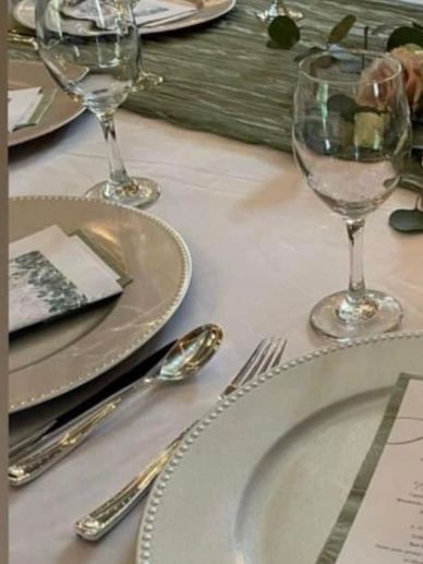 Elegant table setting with glassware, silverware, and decorative plates on a white tablecloth.